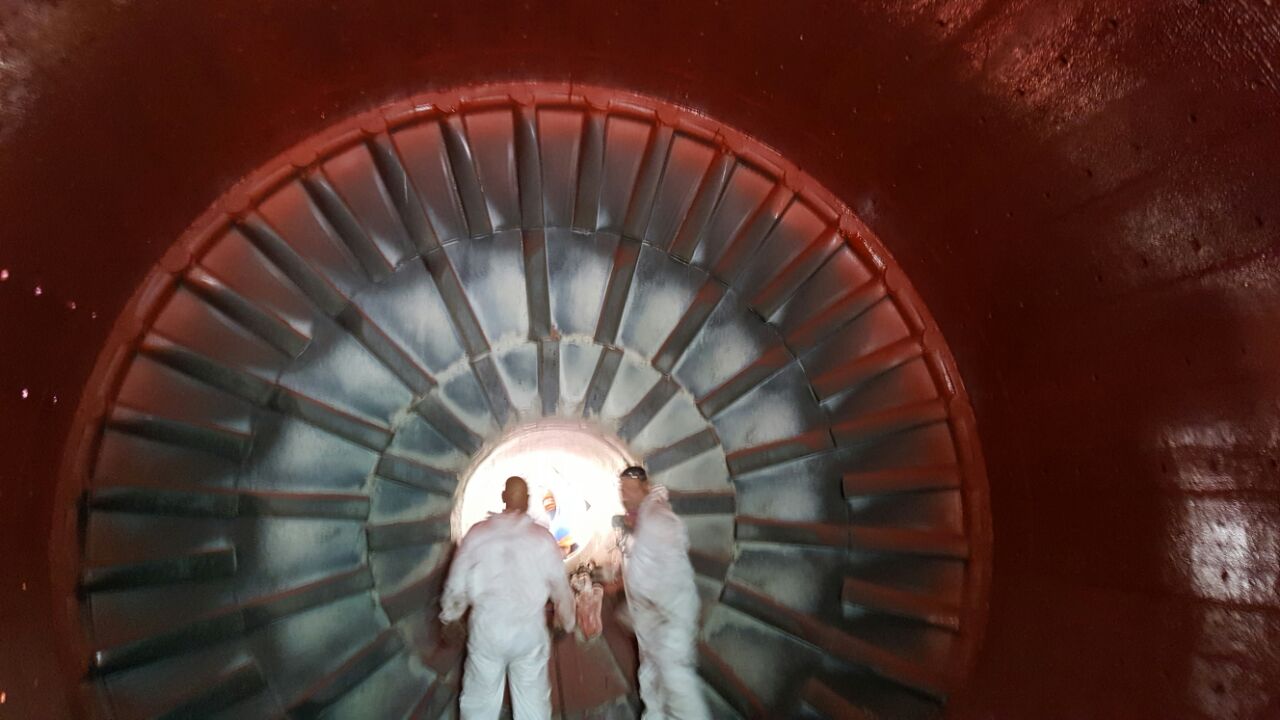 Interior de molino SAG con revestimiento de poliurea rojo completamente aplicado, dos técnicos al centro — Kronos Mining