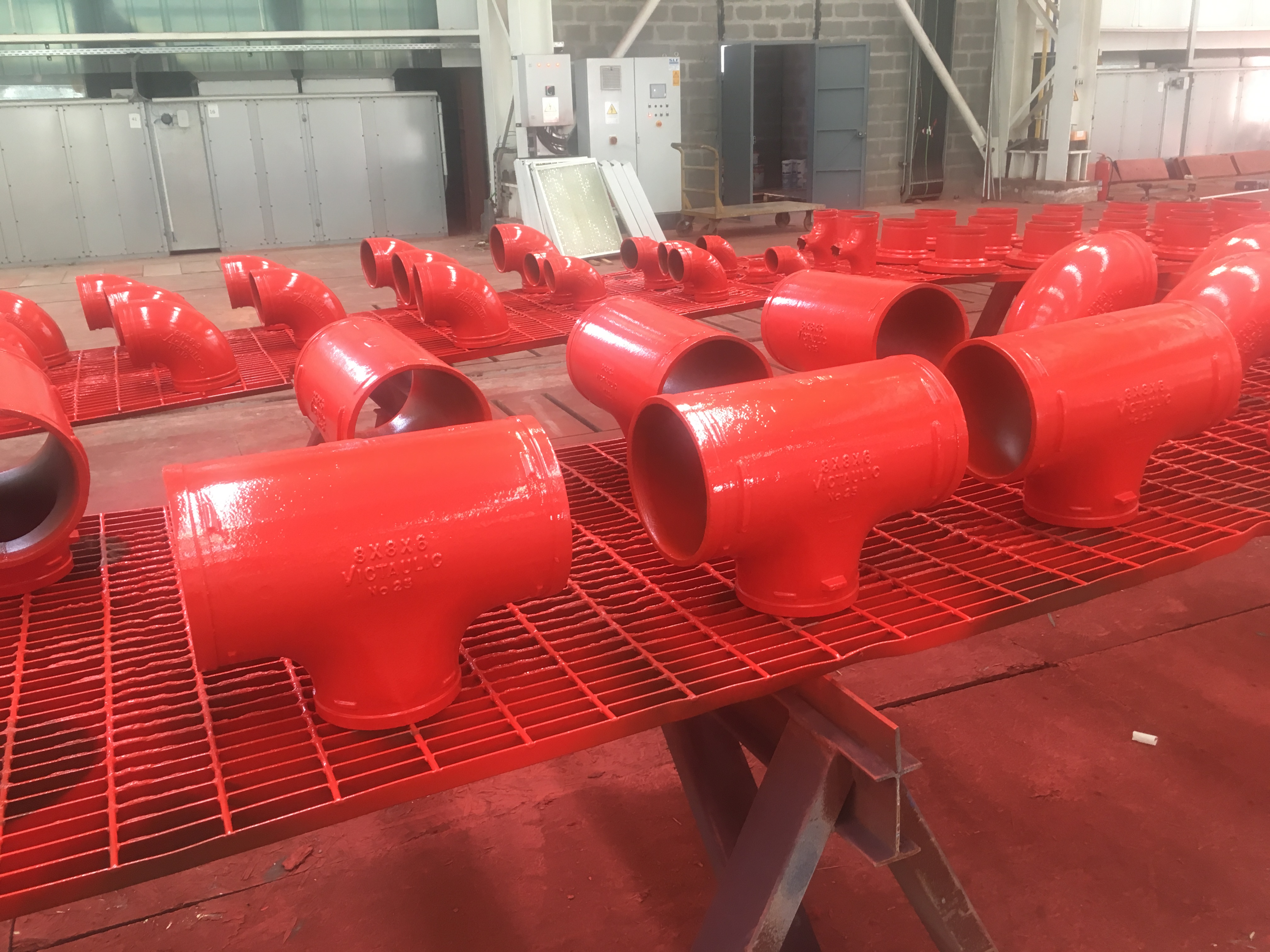Lote de tees y codos de acero pintados en rojo fire fighting sobre mesas de taller industrial — Kronos Mining