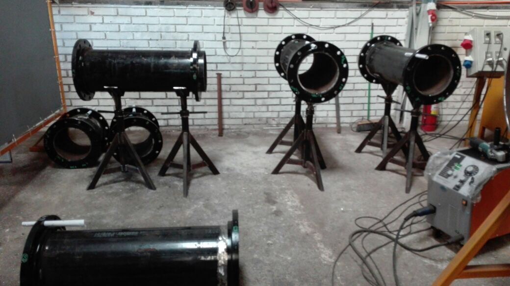 Seis spools terminados con flanges en acero negro alineados en taller, listos para pintura